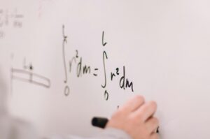 Person writing math equations on a whiteboard, focusing on integrals and formulas.